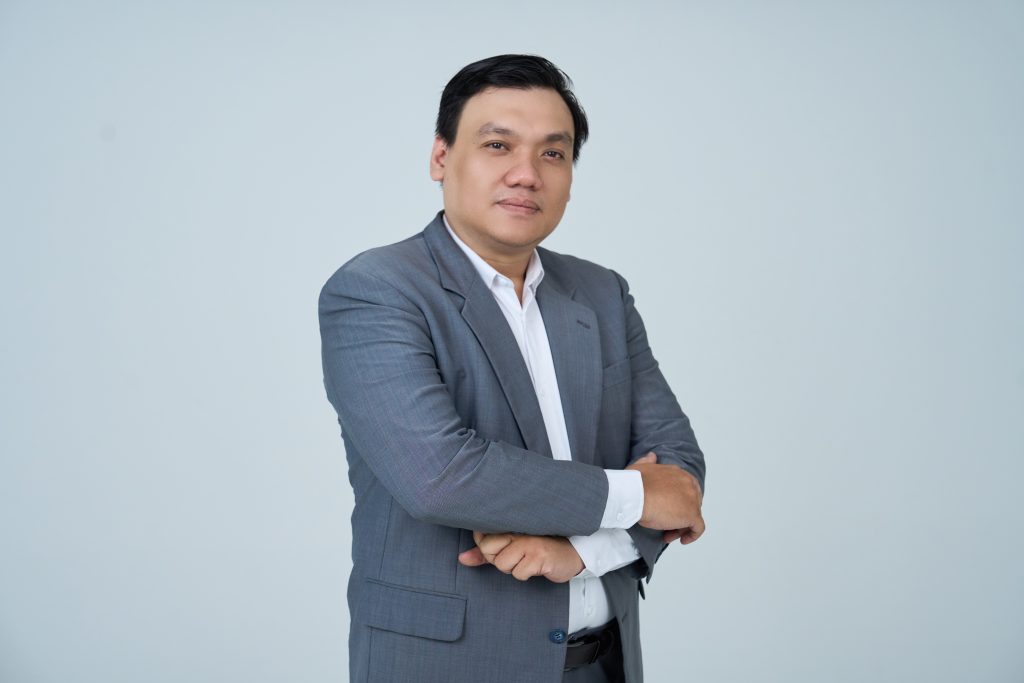 Nguyễn Chiến Trường mặc vest xám, khoanh tay trước ngực, chụp trong phòng studio nền sáng.