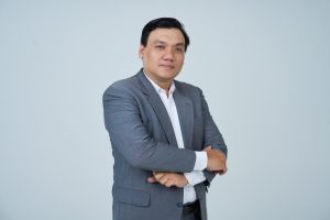 Nguyễn Chiến Trường mặc vest xám, khoanh tay trước ngực, chụp trong phòng studio nền sáng.