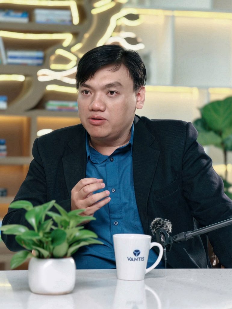 Nguyễn Chiến Trường nói chuyện tại bàn có micro, phía sau là giá sách hình cây phát sáng.