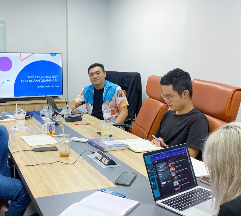Buổi họp quanh bàn gỗ, phía sau là màn hình chiếu "Triết học đạo đức cho ngành quảng cáo".
